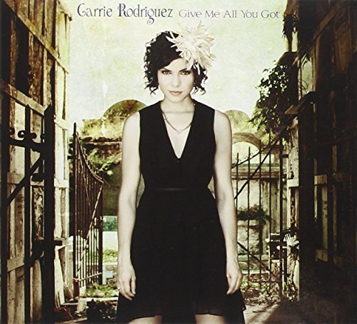 "Album cover featuring a woman in a black dress standing between old buildings."