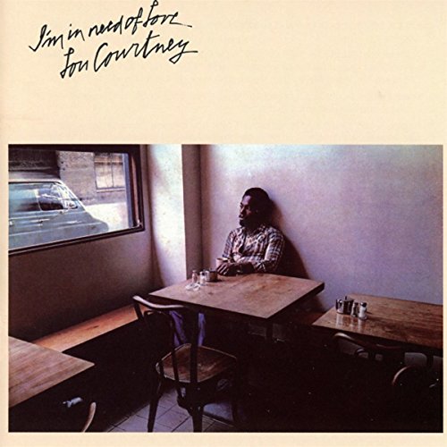 "Album cover with man sitting alone at a diner table, beige background."
