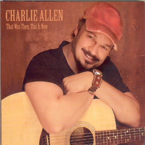 "Man in a red cap holding an acoustic guitar, smiling, on a brown background."