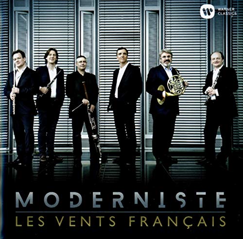 "Five men in suits holding various wind instruments stand before a metal wall."
