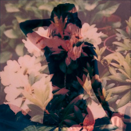 A woman sits surrounded by flowers, with her face obscured by her hair.