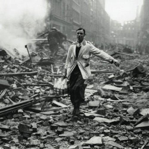 Black and white image of man walking through rubble-strewn street with debris and smoke.