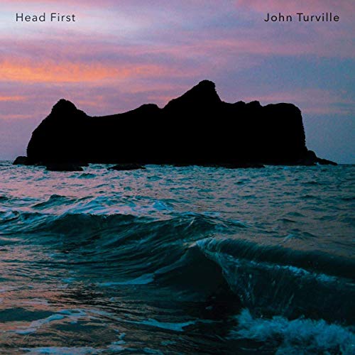 "Album cover with a large rock formation in the ocean at dusk."