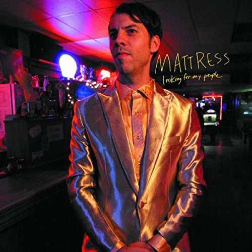 Man in shiny gold suit stands in dimly lit bar with neon lights.