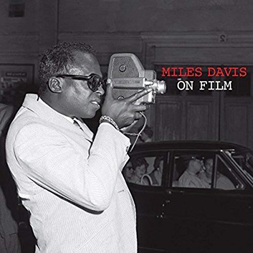 Black and white image of Miles Davis holding a movie camera, with text overlay.