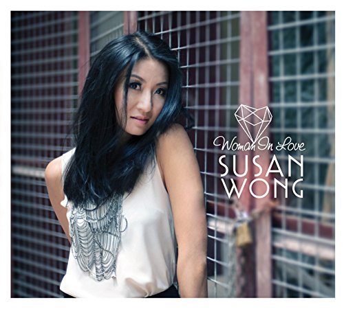 "Album cover featuring a woman with long black hair standing by a metal gate."