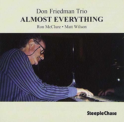 "Album cover with a man playing piano, wearing glasses and a blue striped shirt."