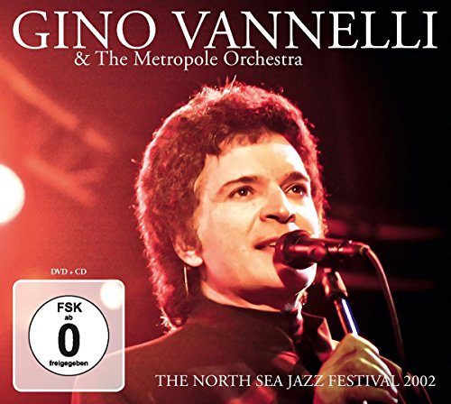 Gino Vannelli singing into a microphone, with red stage lighting in the background.