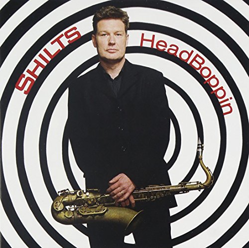 Man in black suit holding saxophone, standing in front of spiral design, album cover.