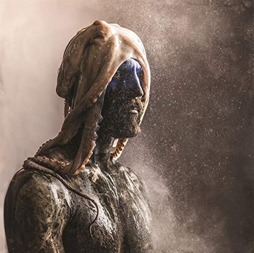 "Man covered in dust, with galaxy-patterned face, against a dusty brown background."