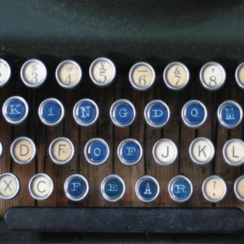 Vintage typewriter keys with white and blue buttons, some highlighted in blue, on a wooden base.