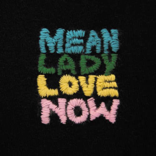 "Black fabric with colorful embroidered text reading 'MEAN LADY LOVE NOW' in pastel colors."
