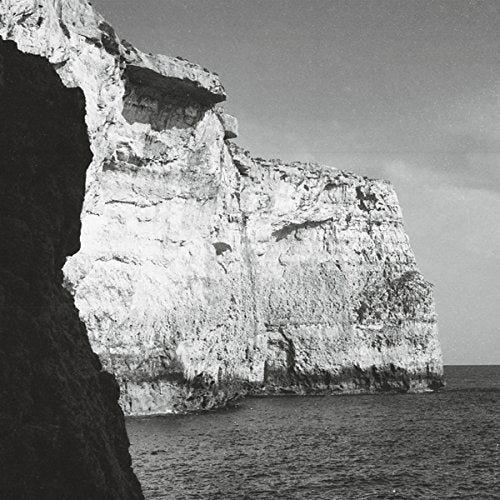 "Black and white photograph of a large, rugged cliffside beside the ocean."