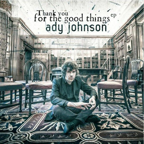 "CD cover with man sitting on ornate carpet in a library-like setting."