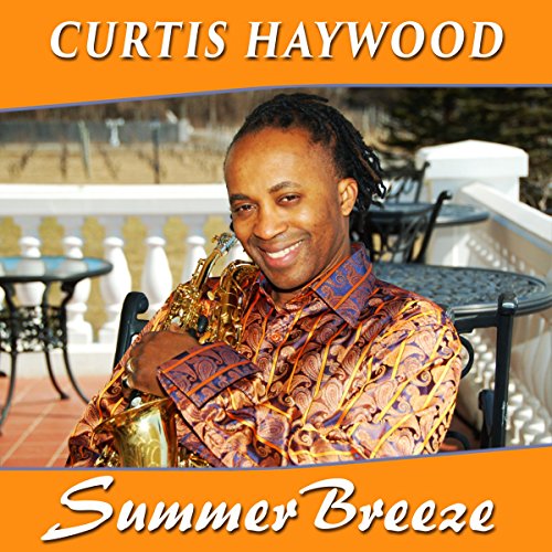 Man holding a saxophone, wearing a patterned shirt, on a patio with tables.