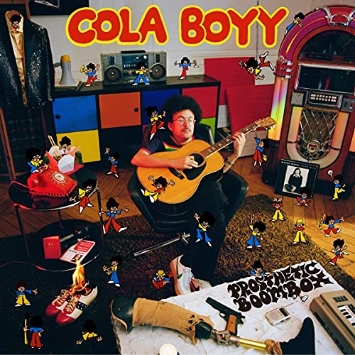 Man playing guitar surrounded by cartoon characters and music equipment in a cluttered room.
