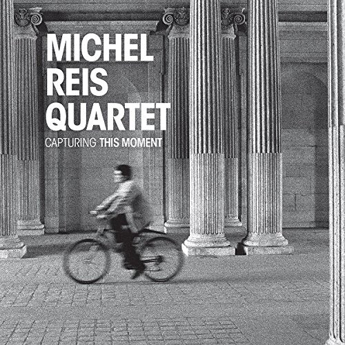 Black and white album cover with a person riding a bike between stone columns.
