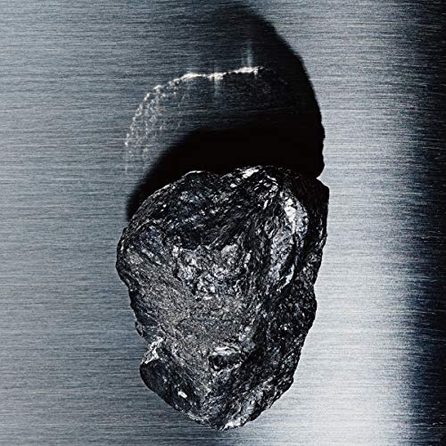 A dark, rough rock casts a shadow on a brushed metal surface.