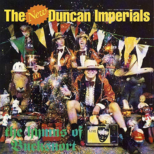 "CD album cover with men in costumes, surrounded by dolls and festive decorations."