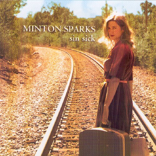 Woman stands on train tracks with suitcase, surrounded by trees, on a music album cover.