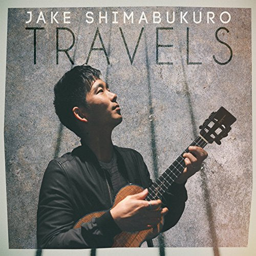 Man holding ukulele, looking up, against a concrete background, with album title "Travels".