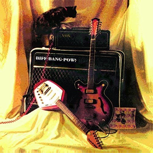 "Album cover with guitars, amplifier, and cat on yellow fabric background."