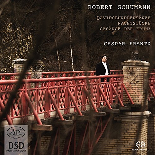A man in a black suit stands on a red metal bridge.