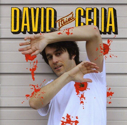 Man in white shirt with red splatters, posing against a gray garage door.