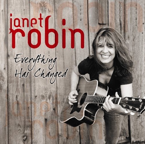 "Album cover with a smiling woman holding a guitar against a wooden background."
