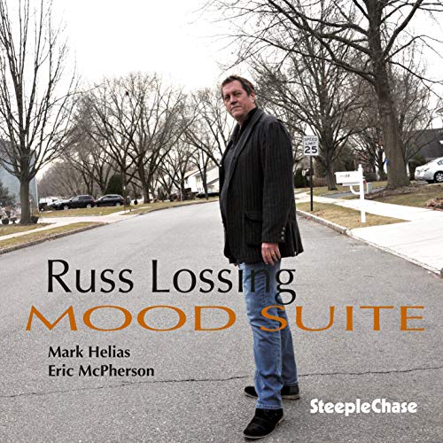 Man in dark coat and jeans standing on a suburban street, album cover.