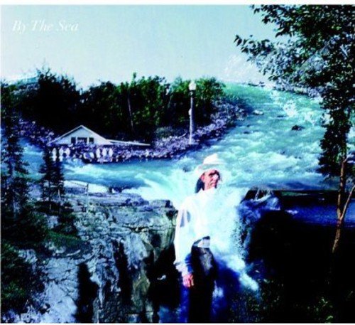 A man in a white hat and shirt stands in a waterfall.