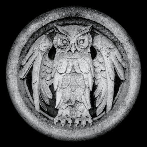 A grayscale image of a stone owl carving within a circular border on a dark background.