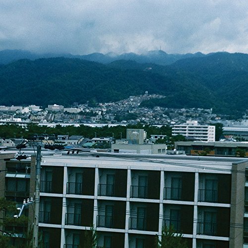 The image depicts a cityscape with a building and mountains. For accessibility purposes, a concise description of the image is: a large building with mountains in the background.