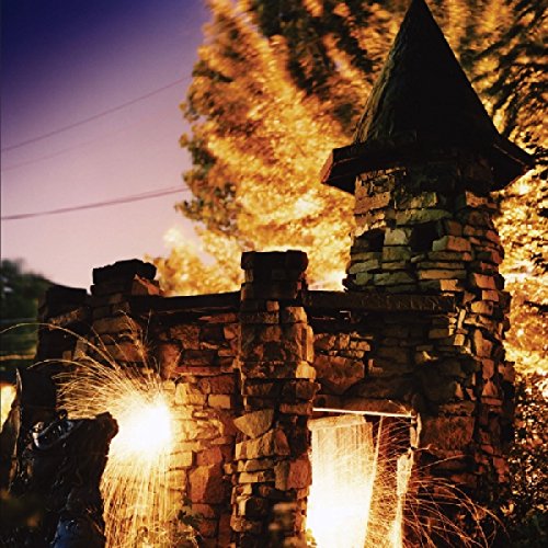 "Stone castle turret with waterfalls and sparks at dusk, surrounded by trees."