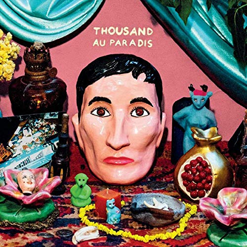 "Vinyl album cover with a large doll's head and various small figurines on a rug."