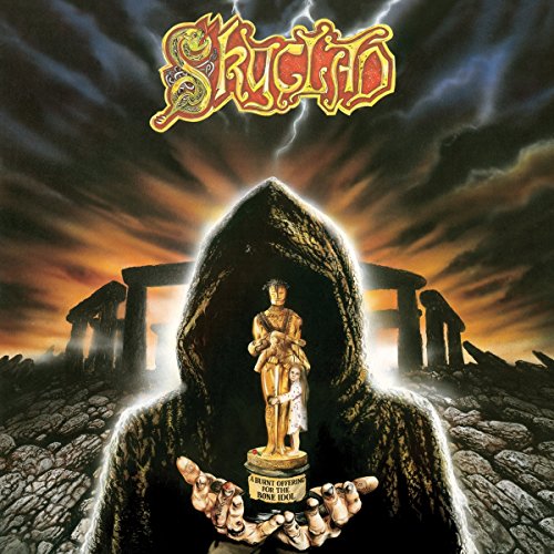 Hooded figure holds a golden statue, with ruins and stormy sky in the background.