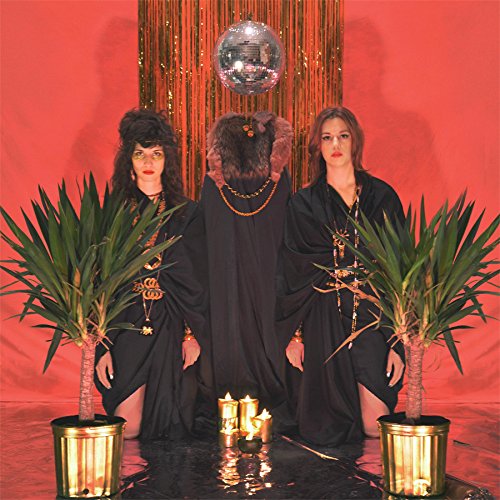 Three people in black stand before a disco ball, flanked by potted plants.