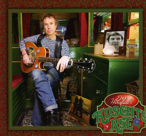 A man sits on a green bench holding a guitar, in a train carriage.