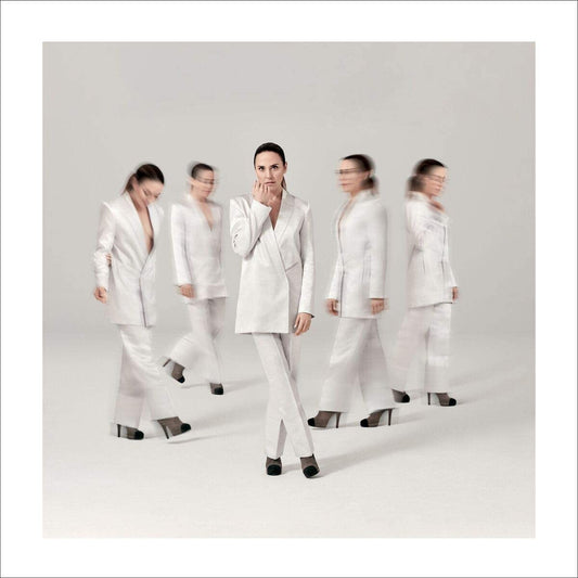 Melanie C in white suit, surrounded by blurred duplicates, against a plain white background.