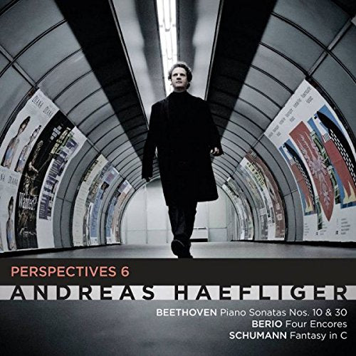 "CD cover with a man in black walking down a tunnel with posters."