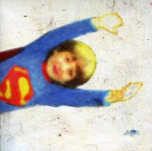 A young child dressed as Superman stands with arms raised against a textured white background.