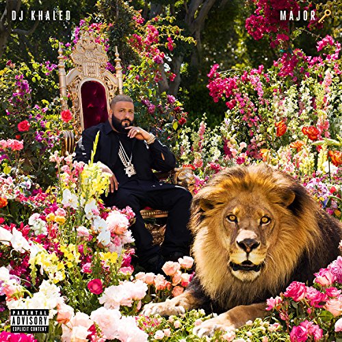 DJ Khaled sits on a throne surrounded by flowers with a lion beside him.