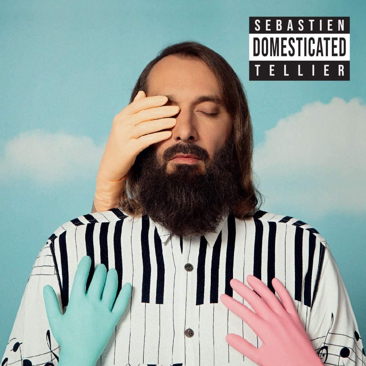 Man with long hair and beard, wearing striped shirt, against a cloudy sky background.
