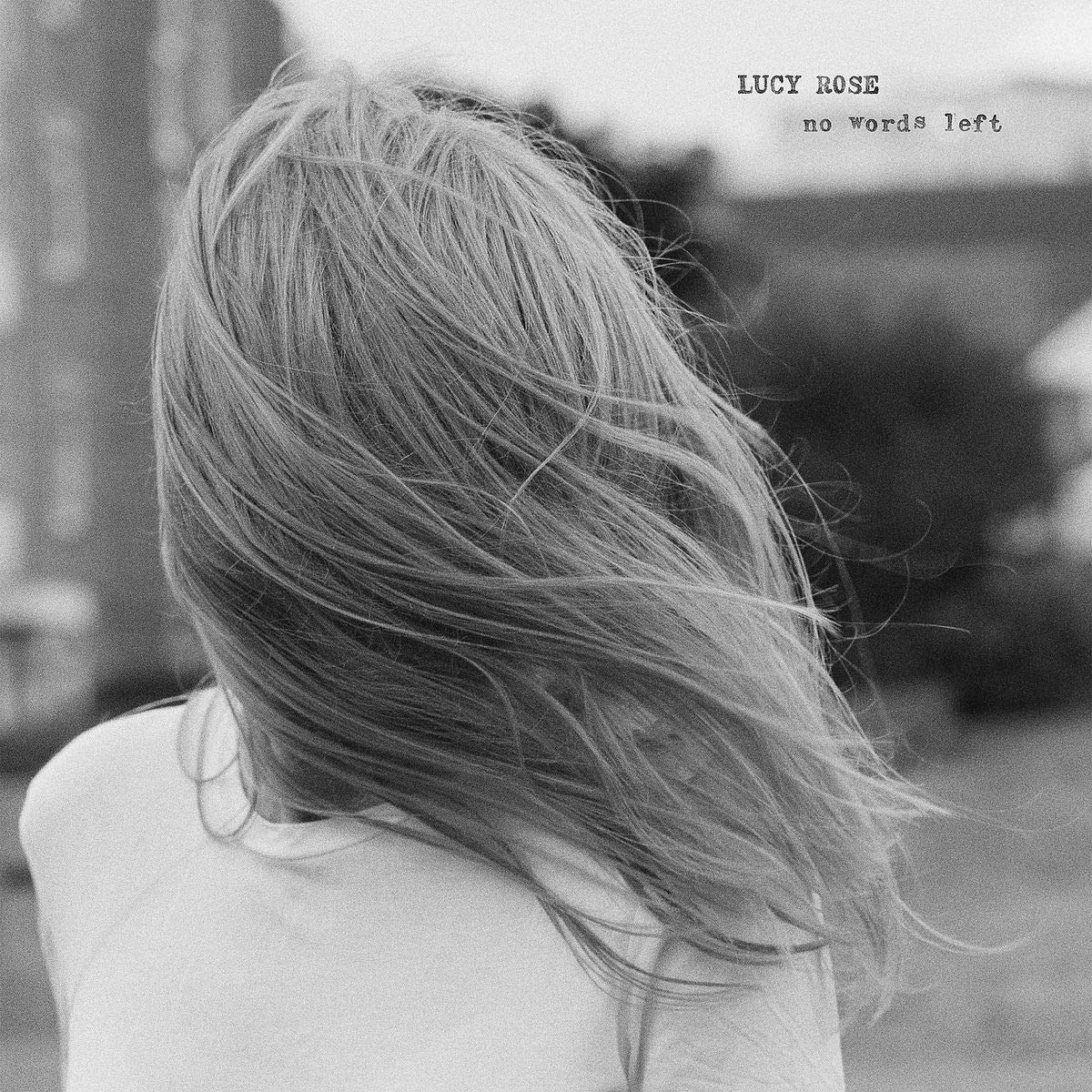 The alt text for the image is: "Black and white album cover with a woman's back to the camera."