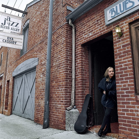 "Woman stands outside brick building with guitar case, 'Live at Blues Alley' text overlay."